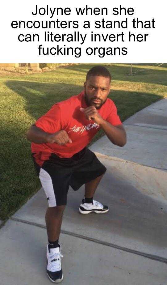 man in red shirt and black shorts standing on sidewalk with his fist in the air