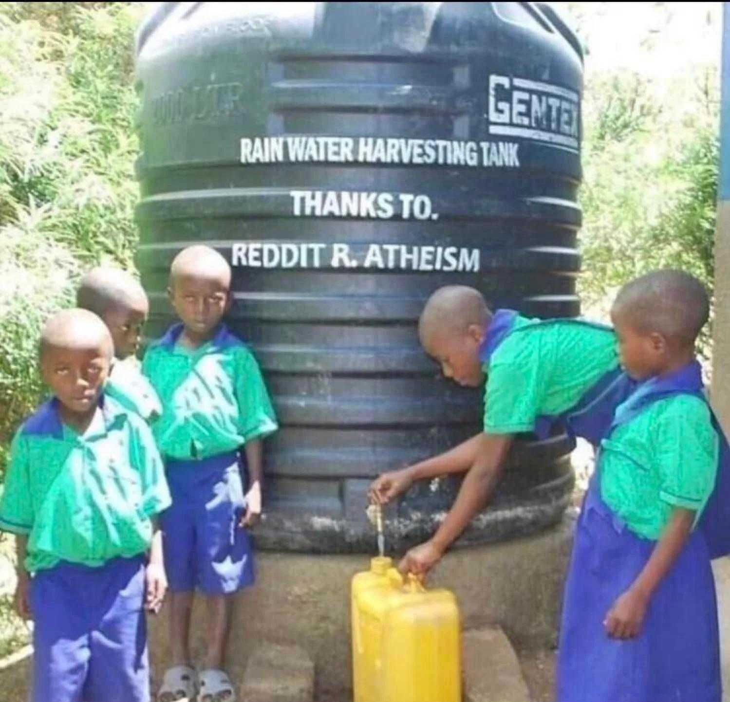 several children in blue uniforms are standing near a water tank