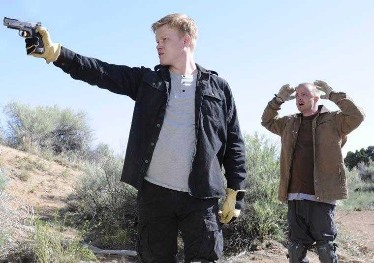 two men in black jackets holding guns in a desert area