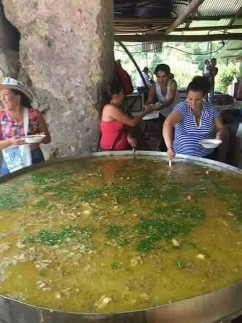 people standing around a large metal pan filled with soup