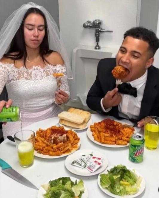 bride and groom eating spaghetti and meat at a table with plates of food