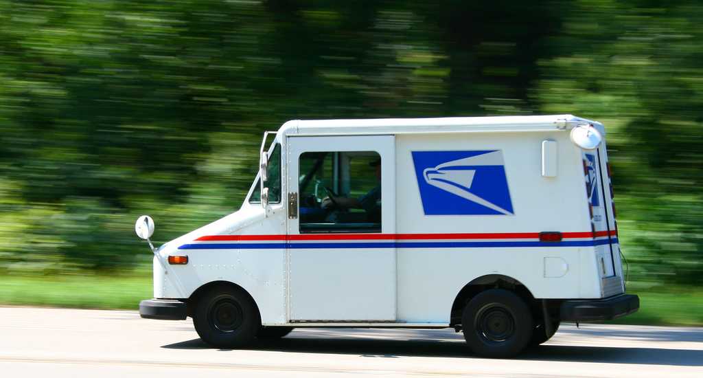 mail truck driving down a road with trees in the background