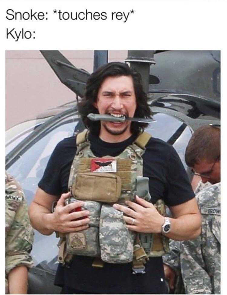 man in camouflage holding a gun in front of a helicopter