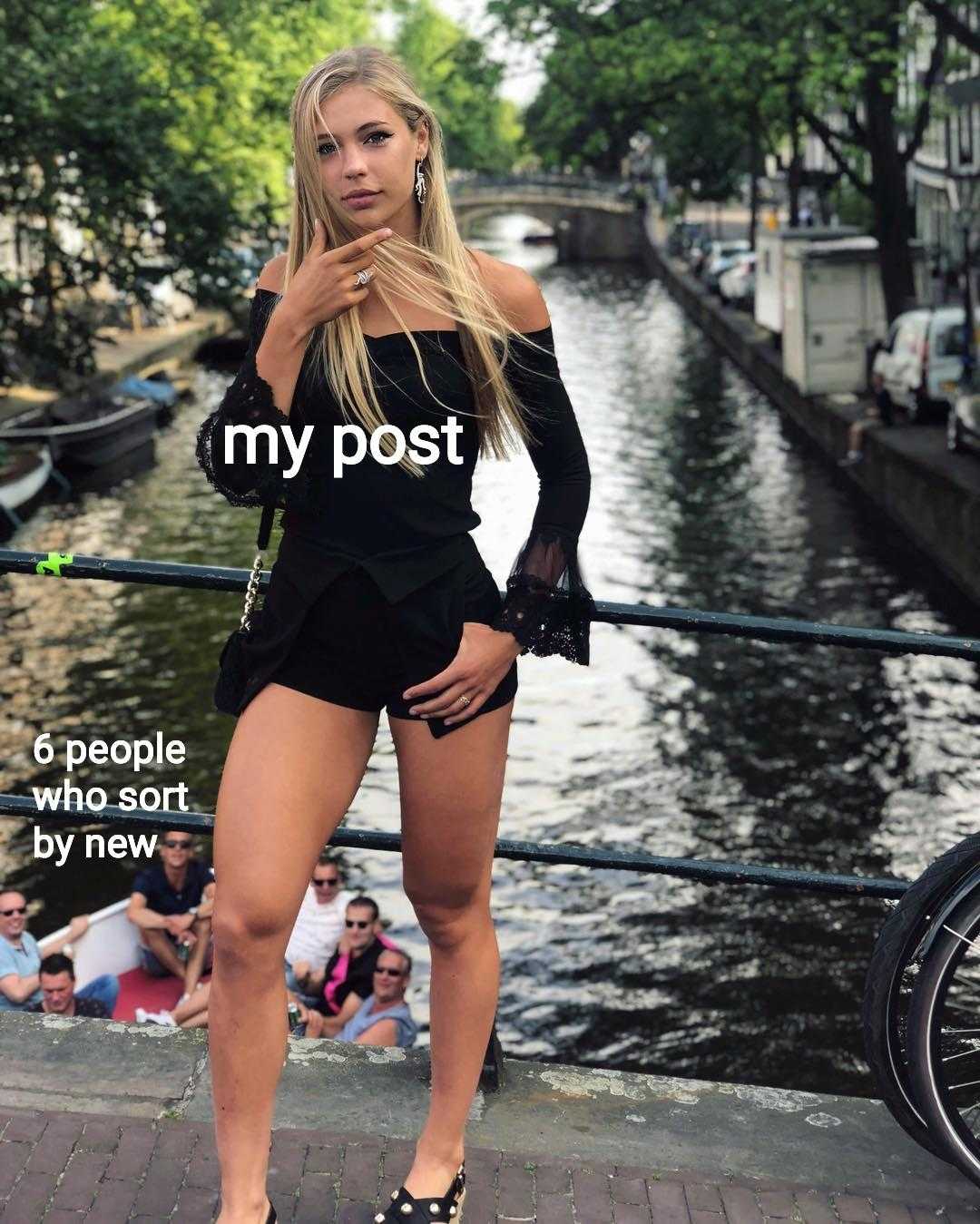 blond woman in black outfit standing on a bridge with a bicycle