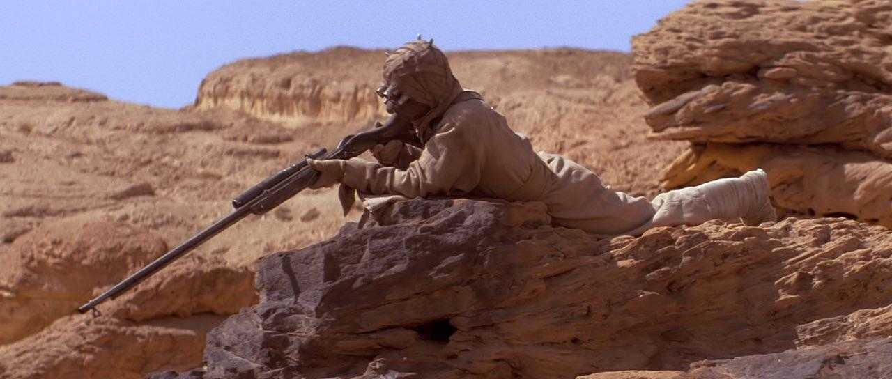 man with a gun sitting on a rock in the desert