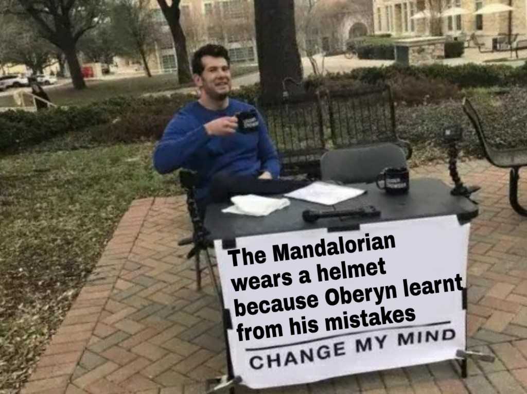 man sitting at a table with a sign that says the mandalarian wears a helmet because obeerny learn from his mistakes change my mind