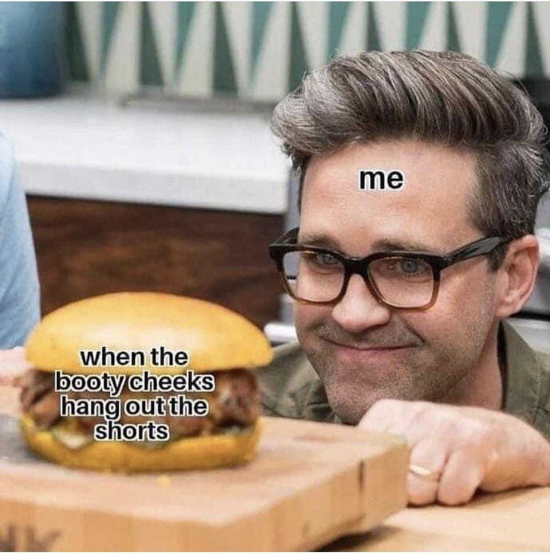 man with glasses looking at a hamburger on a cutting board