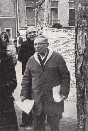 man in a coat and glasses walking down a sidewalk