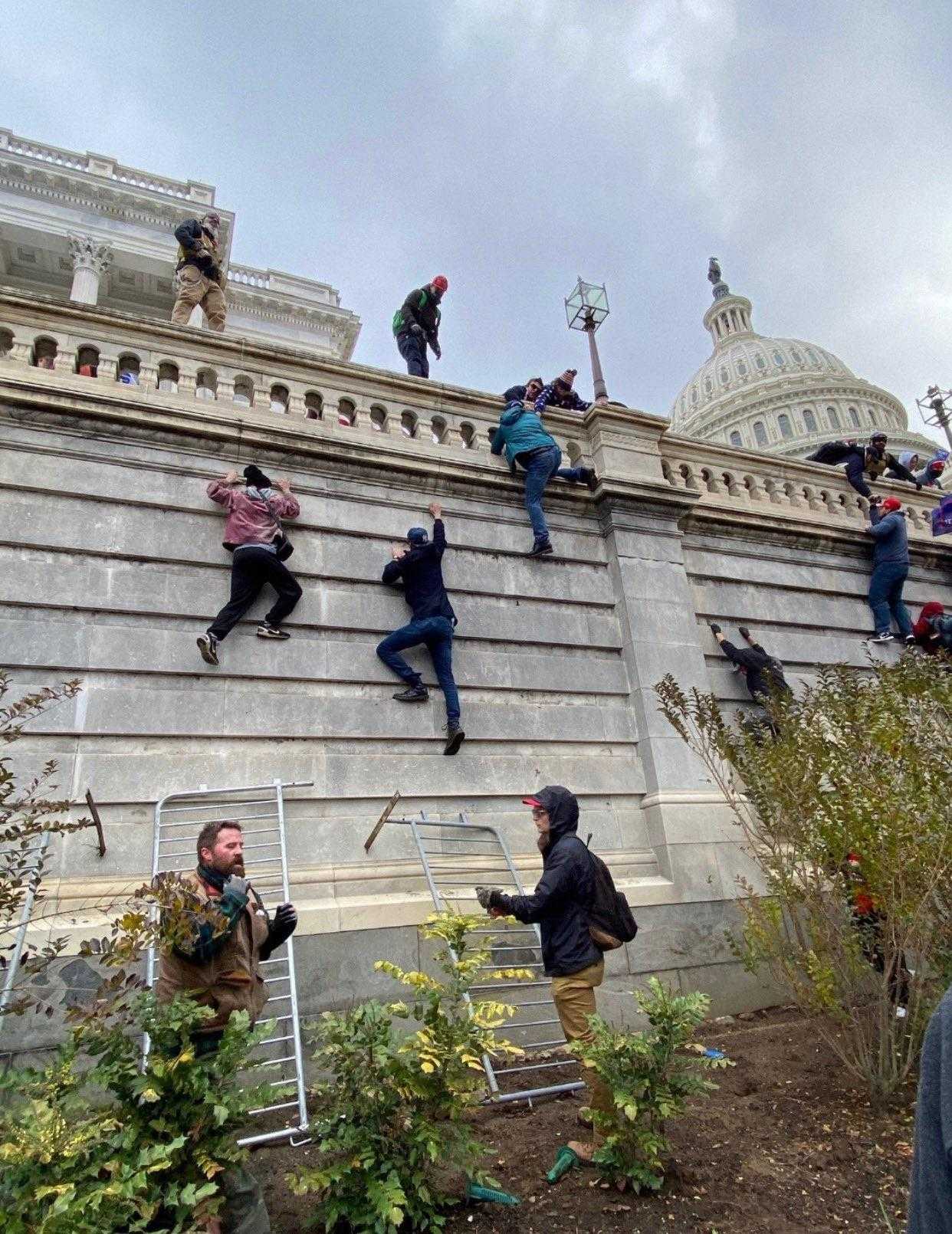 people climbing up a wall with a building in the background