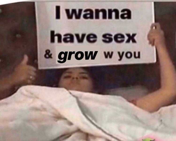 woman laying in bed holding up a sign that says i wanna have sex and grow w you