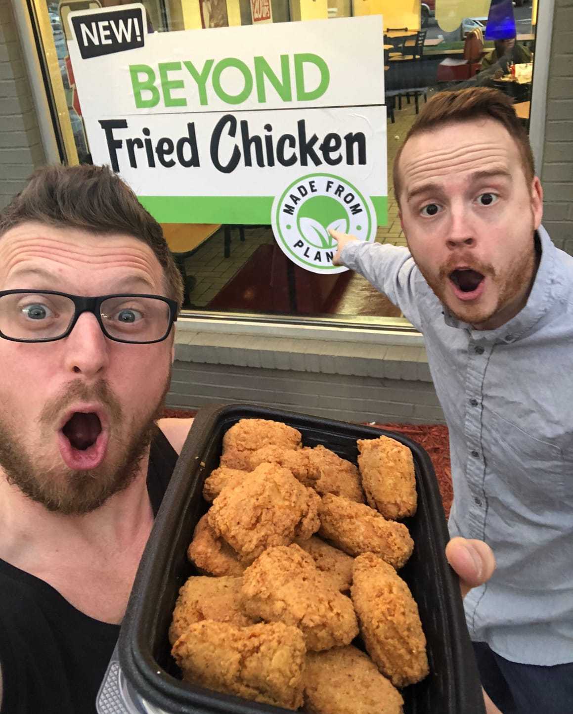 two men holding a tray of fried chicken outside of a store