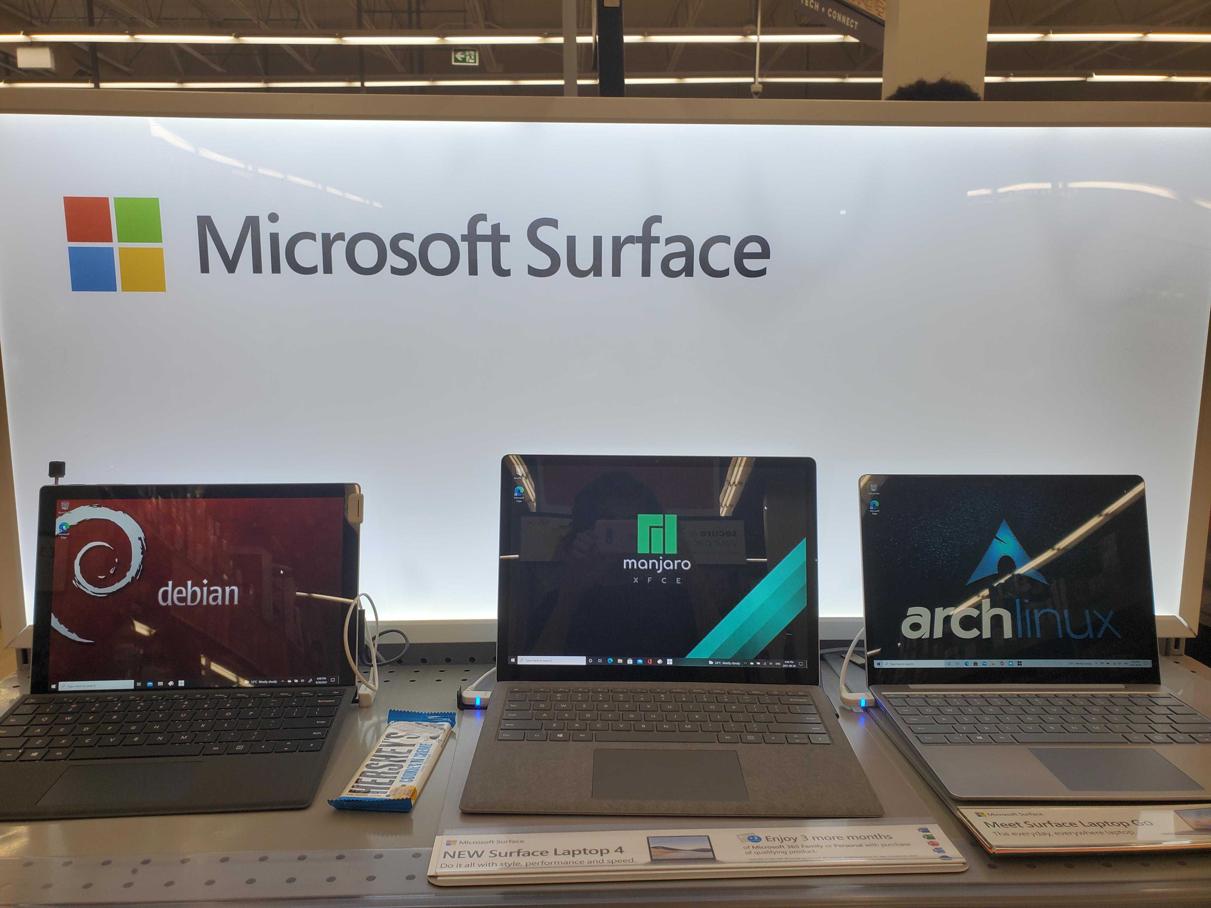 three laptops are on a table with a microsoft surface sign