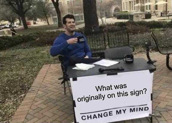 man sitting at a table with a sign that says, what was originally on this sign? change my mind