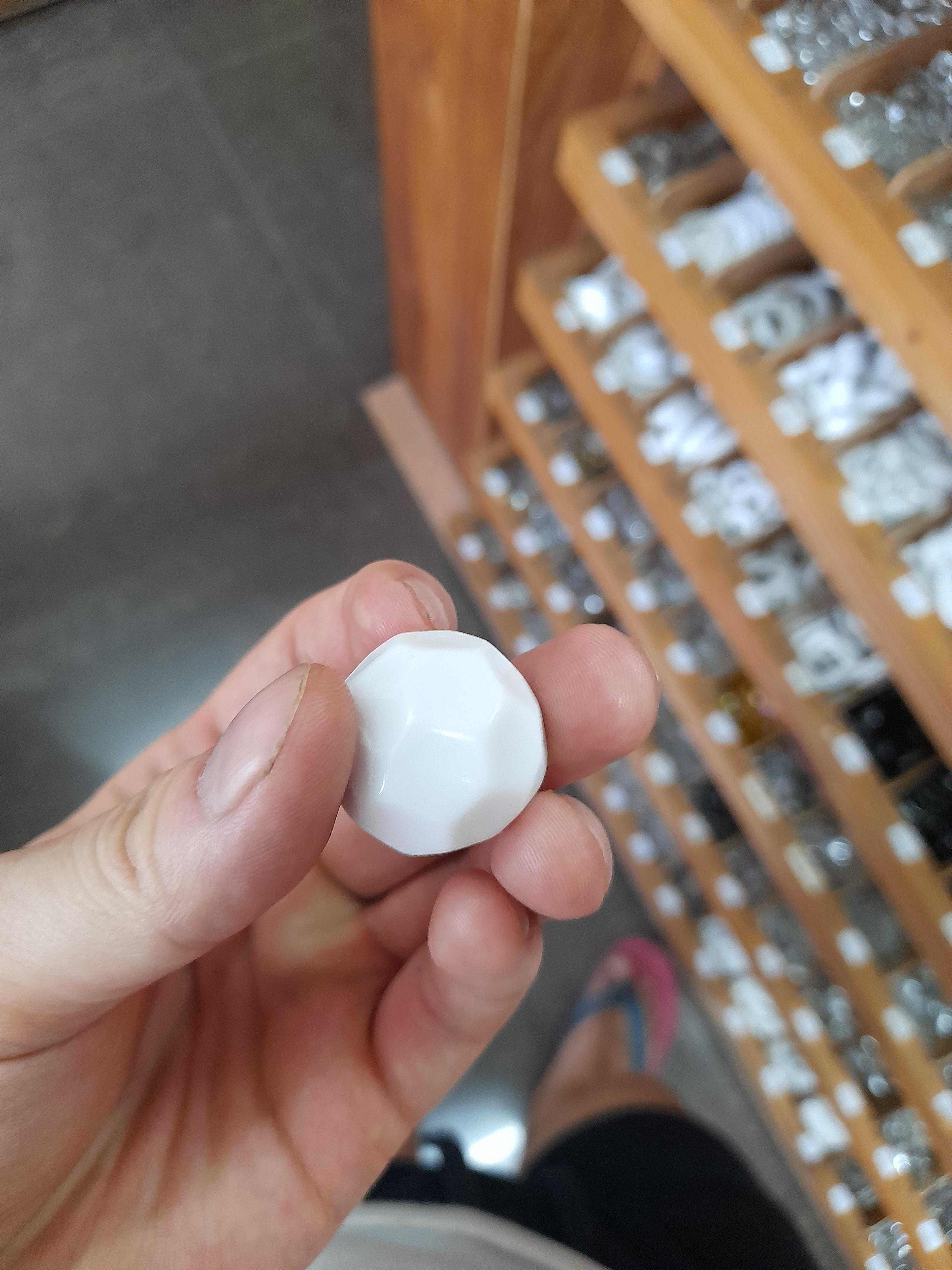 someone holding a white object in their hand in front of a shelf of glass bottles