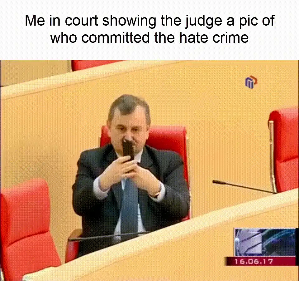 man in a suit sitting in a courtroom with a cell phone