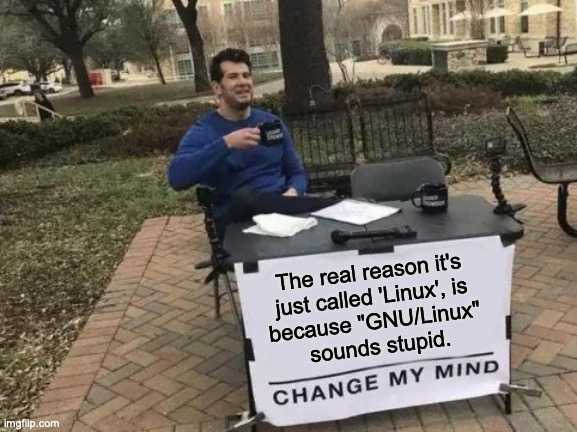 man sitting at a table with a sign that says, the real reason it ' s just called linux is because vyn / linux sounds stupid