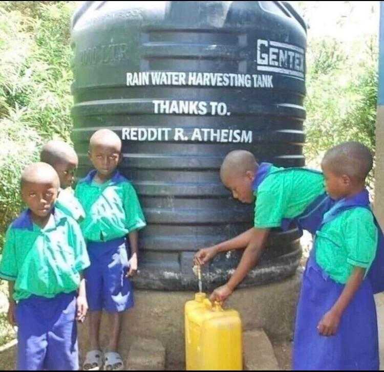 several children in green shirts are standing near a water tank