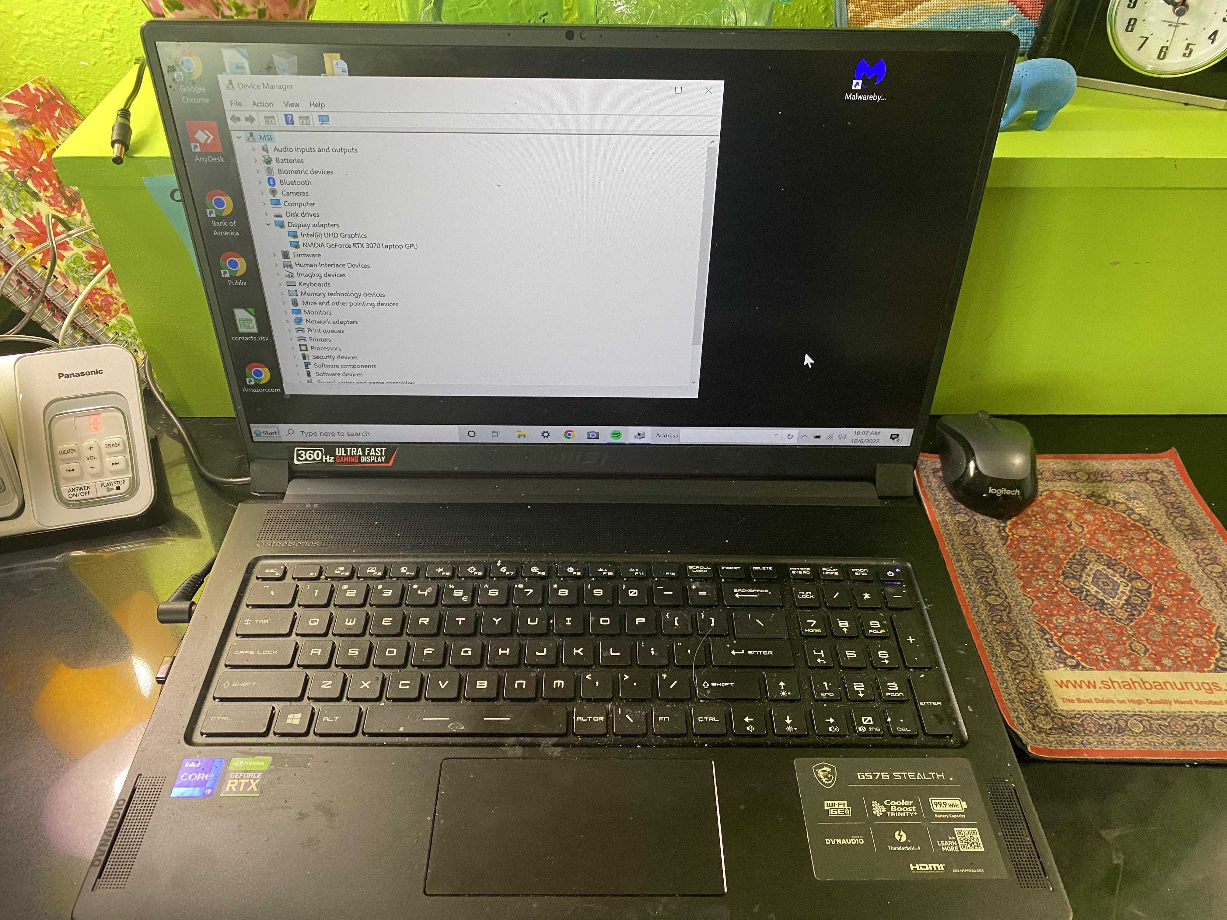 laptop computer sitting on a desk with a clock and a phone