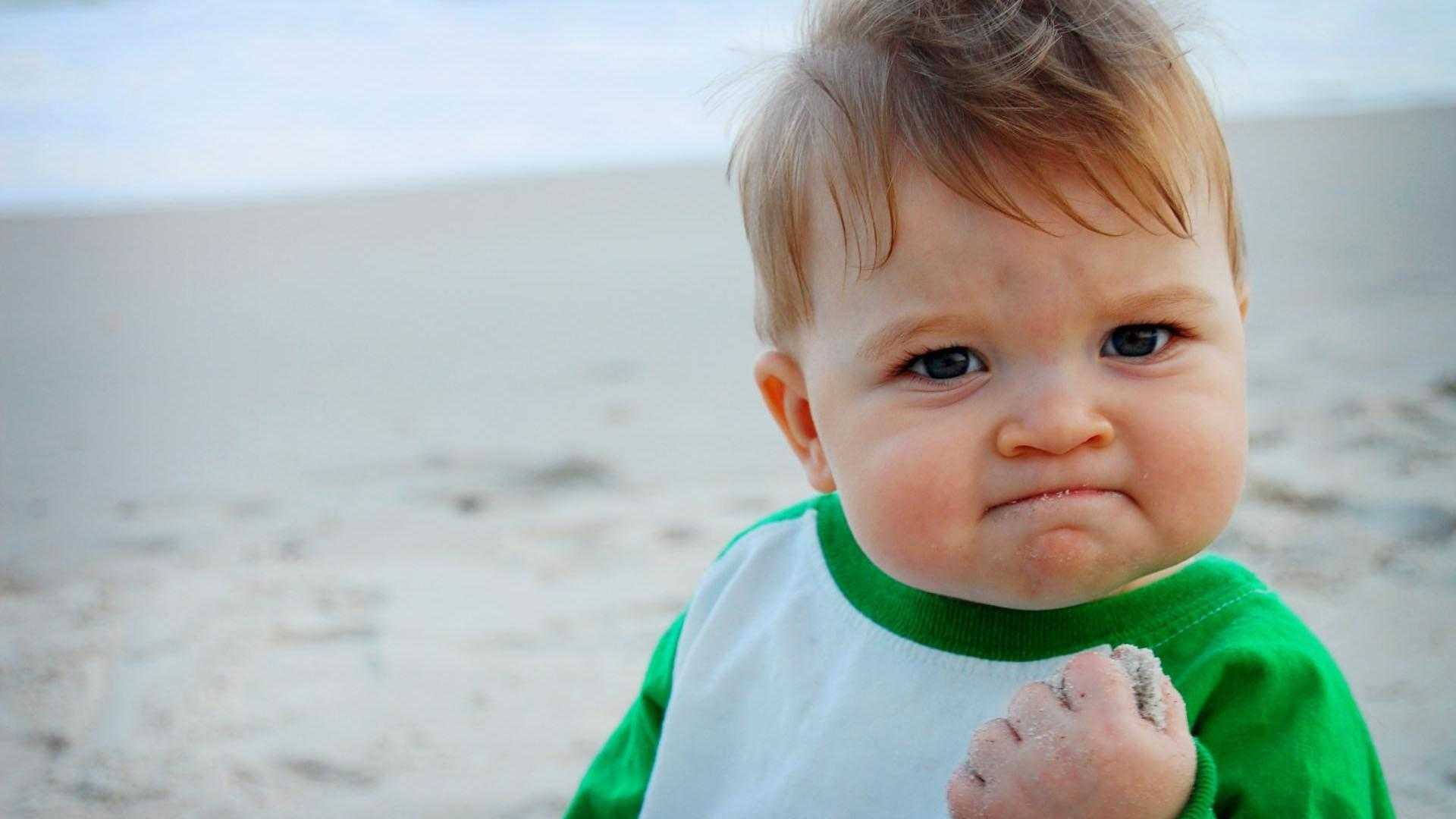 there is a baby that is standing on the beach with a sand in his hand